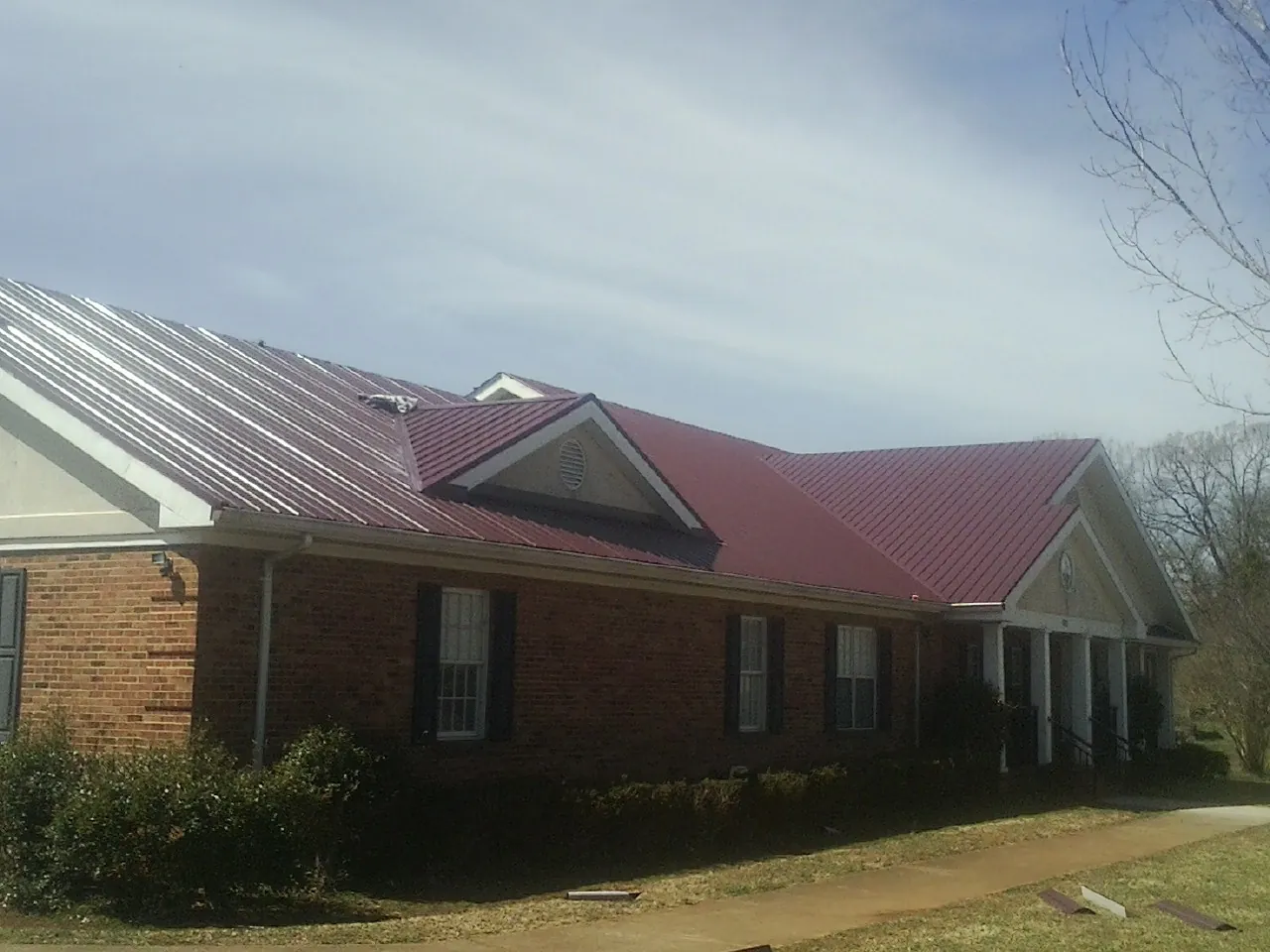 Red metal roof with gabled entries on a long brick building, from a Hail Damage Roof Repair job in Broomes Island