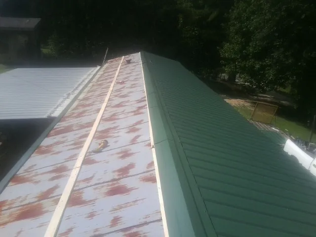 Old rusted panels beside newly installed green metal roofing — Wind Damage Roof Repair by Roofing Brothers in Broomes Island