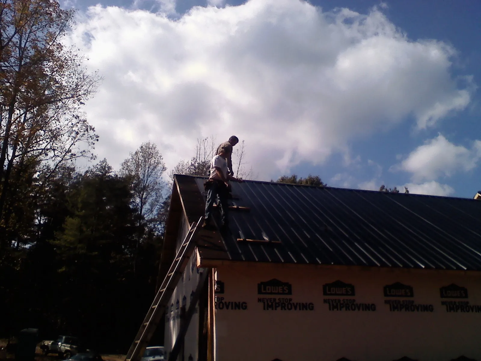 Roofer fastening dark metal panels high against a cloudy sky, from a Roof Inspection job in Broomes Island
