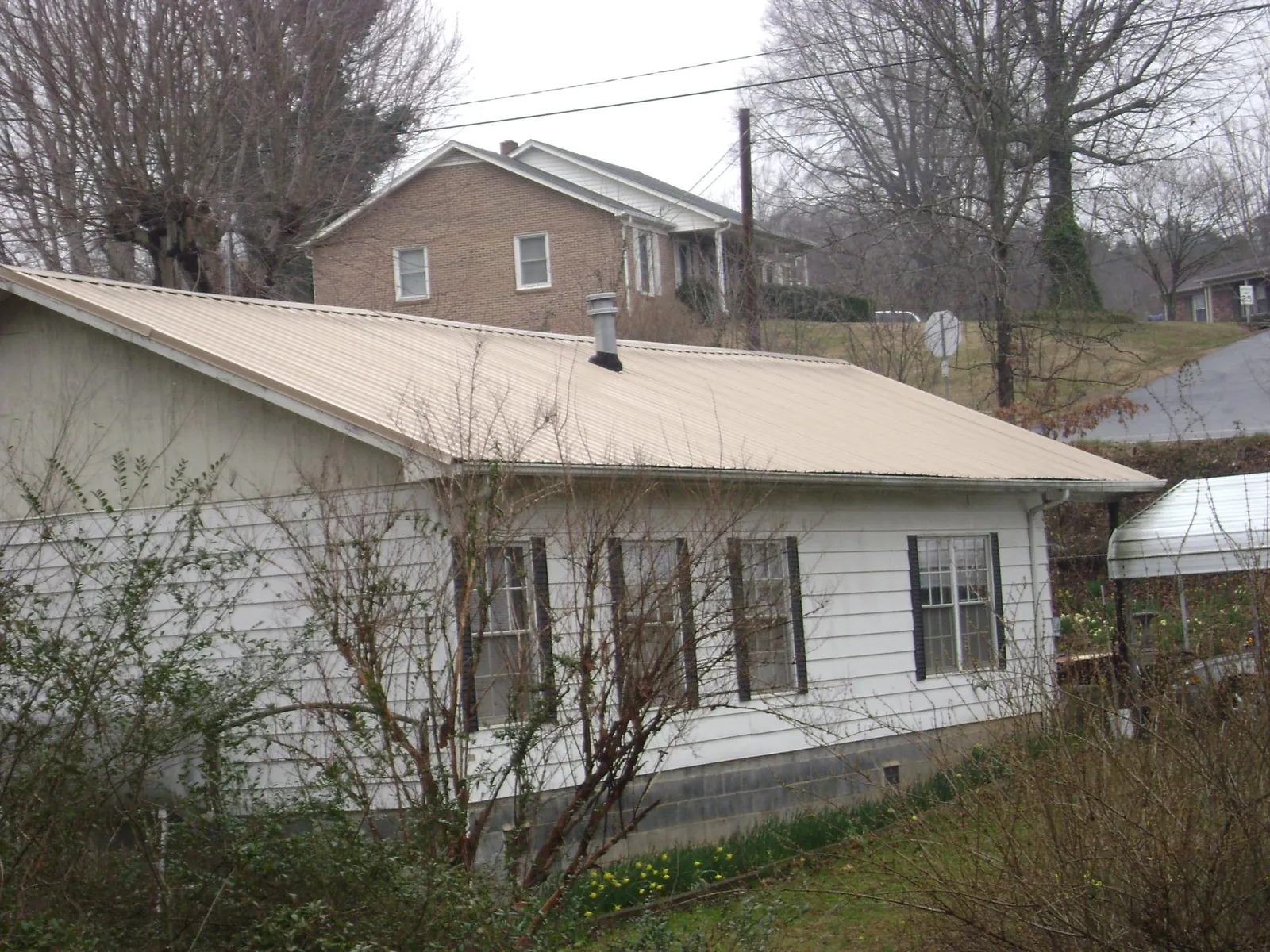 Tan metal roof on a white sided house set into a hillside — Commercial Roofing by Roofing Brothers in Broomes Island